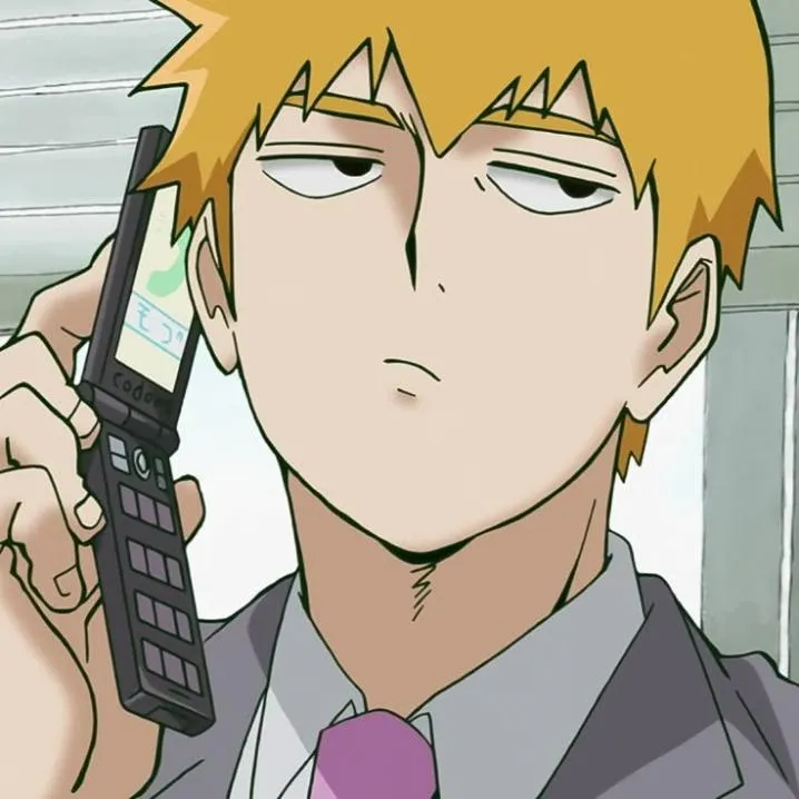 Anime PFP #44: Reigen Arataka with blond hair and a half lidded stare holds a flip phone to his ear in a grey suit and pink tie.
