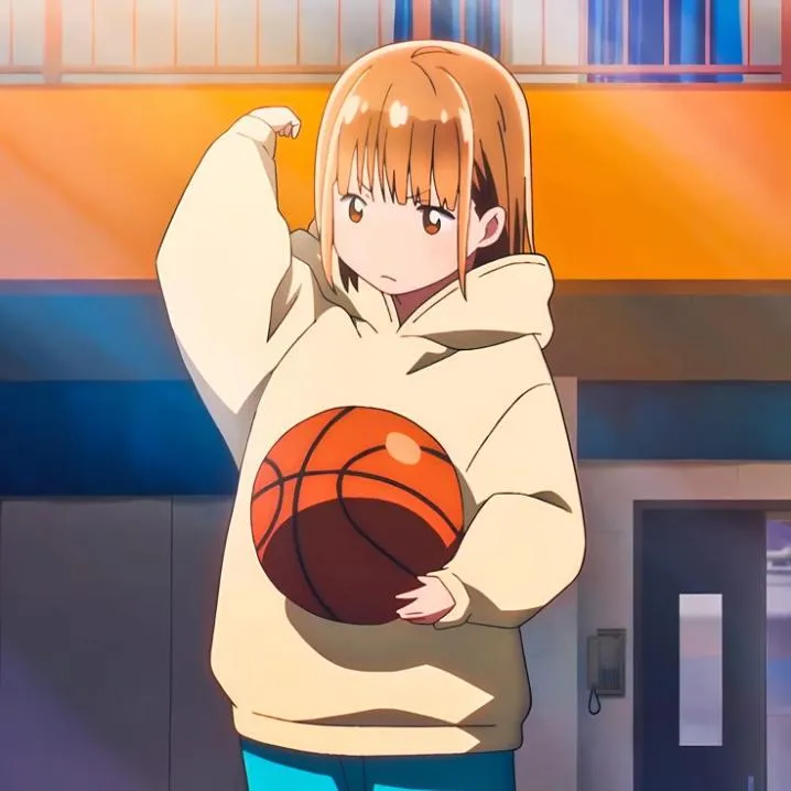 Basketball PFP #20: A girl with light brown hair and bangs in an oversized cream hoodie holds a basketball under her arm in a sunlit gym.