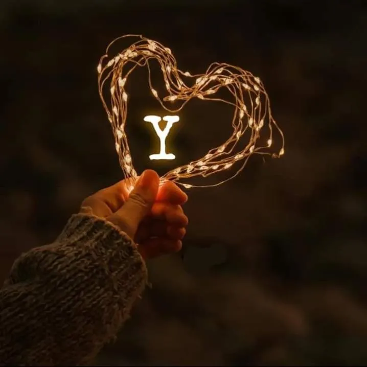 Letter PFP #136: A glowing letter Y sits inside a heart made of warm fairy lights held up in a hand in a knit sleeve.