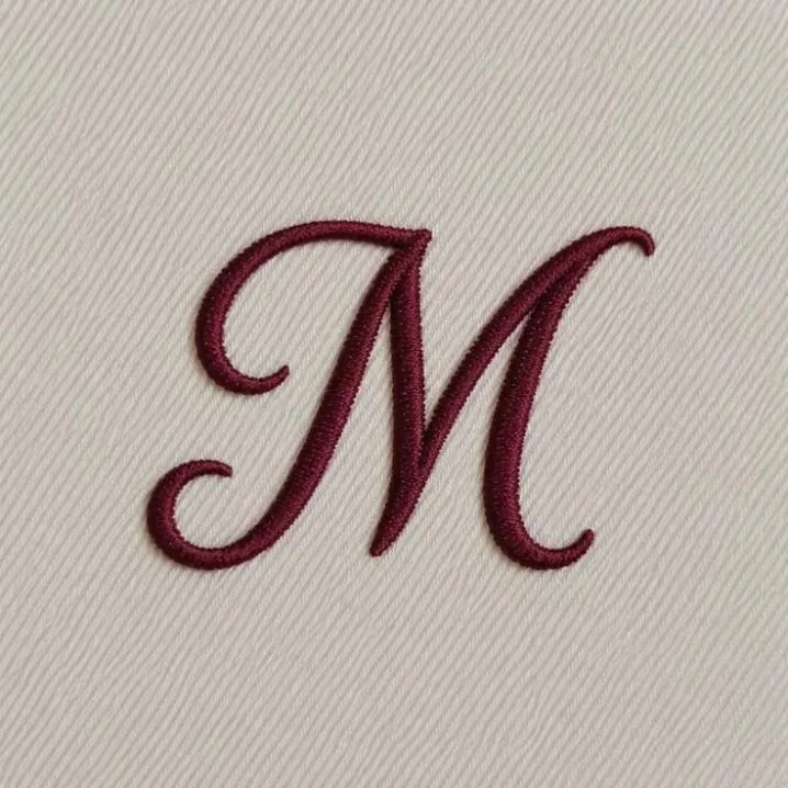 Letter PFP #150: A dark red script letter M is embroidered in thick thread on a cream twill fabric background.