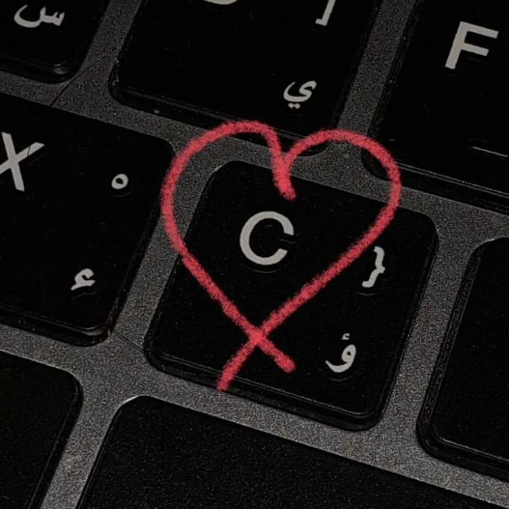 Letter PFP #93: A red heart drawn in marker circles the C key on a black laptop keyboard with Arabic letters on the keys.