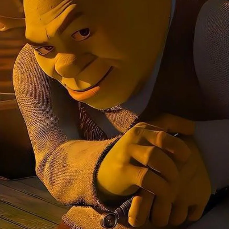 Shrek PFP #13: Shrek leans low over a wooden table in warm golden light, smirking sideways with narrowed eyes while one hand rests on the tabletop.