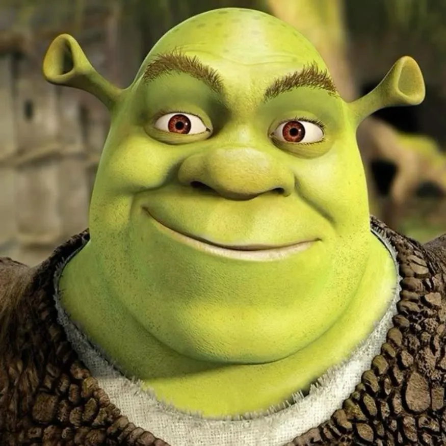 Shrek PFP #20: A close-up of Shrek smiling with brown eyes and raised brows, wearing his brown vest over a white shirt against a blurred background.